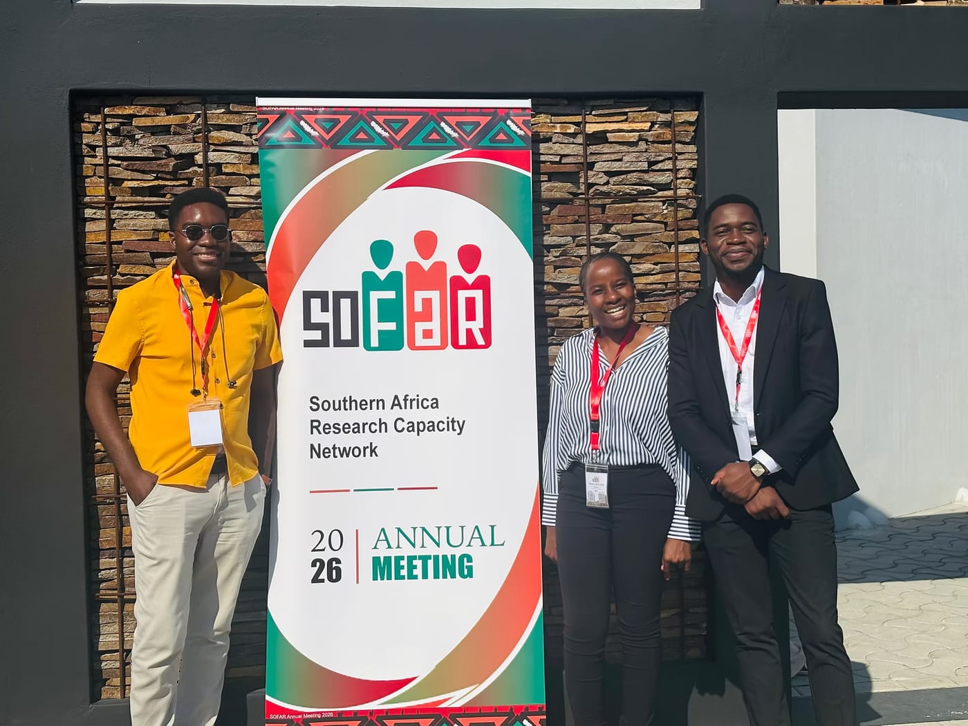 Three researchers standing beside the SOFAR 2026 Annual Meeting banner